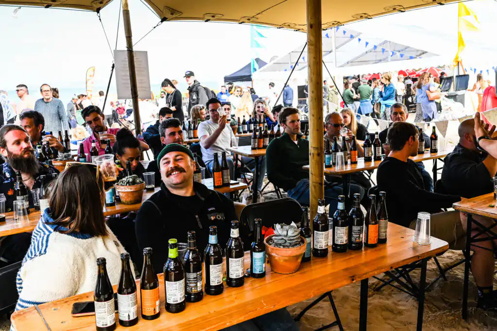People gathered at tables with beer bottles, enjoying the atmosphere at one of the St Ives Food Festival's Drinks Bars.