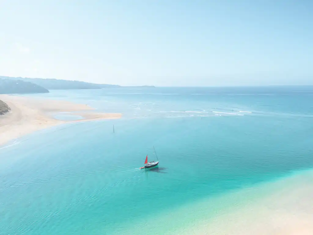 A boat floats in the ocean near Mexico Towans Beach, showcasing the serene beauty of Cornwall's sandy shores.