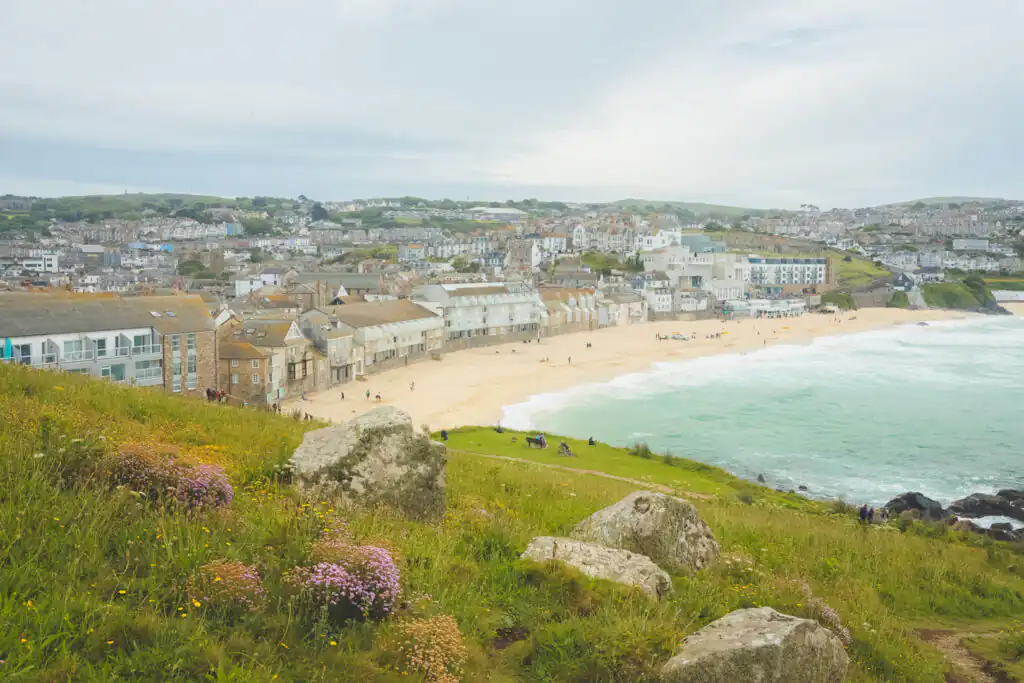 View of Porthmeor Beach, known for surfing, with buildings perched on a hill, capturing the essence of Cornwall's coastline.