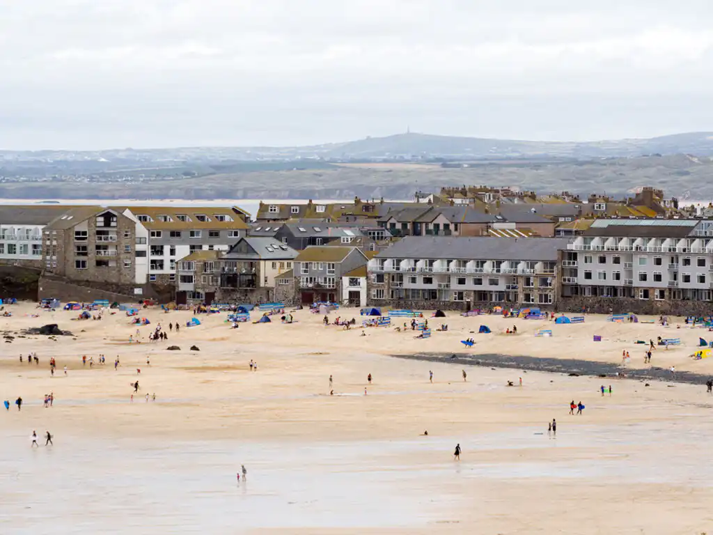 A sunny view of Porthmeor Beach, featuring soft golden sand and gentle waves lapping at the shore.