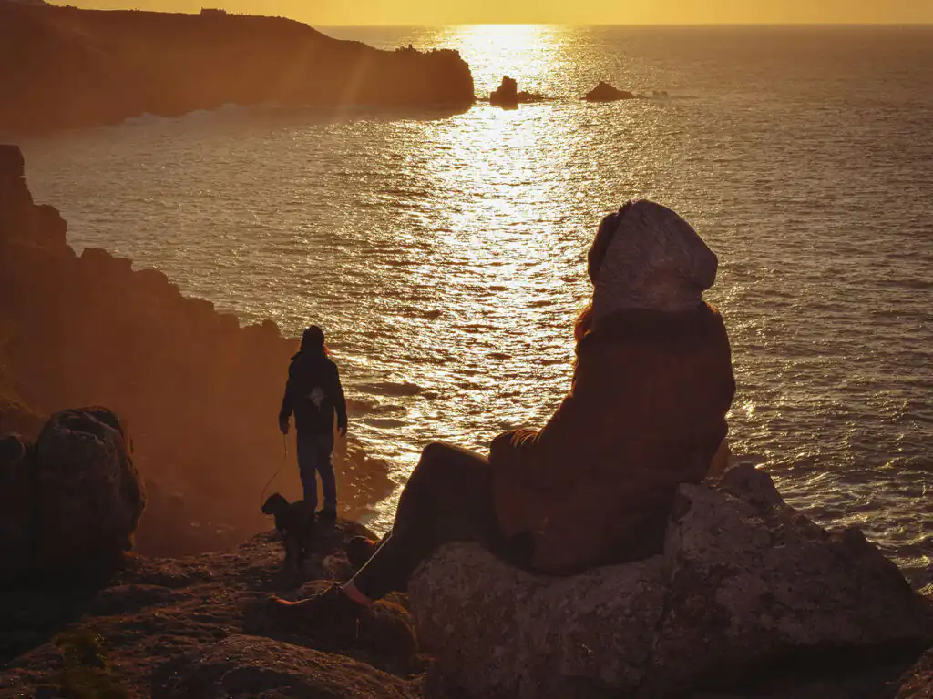 People walking their dog whilst gazing at the ocean from a cliff, enjoying a scenic view during their holiday at a February half term cottage in Cornwall.
