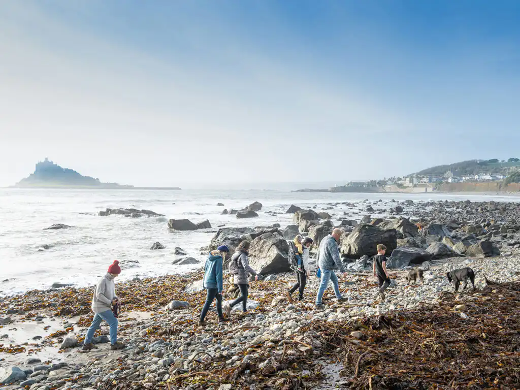 A group of people walks their dog along Marazion beach with St Michael's Mount visible in the background, visiting from their dog friendly cottage in Cornwall.