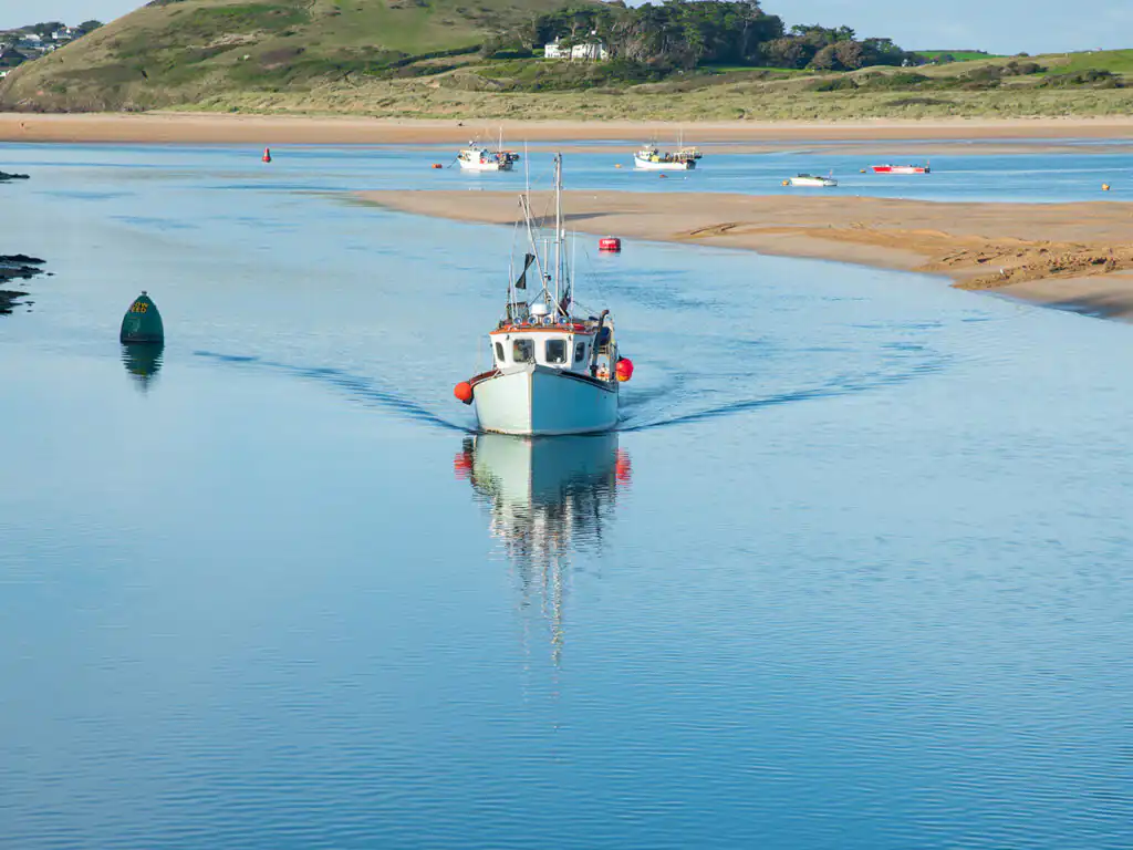 A fishing boat entering Padstow Harbour, surrounded by calm waters and scenic views of the Camel Estuary.
