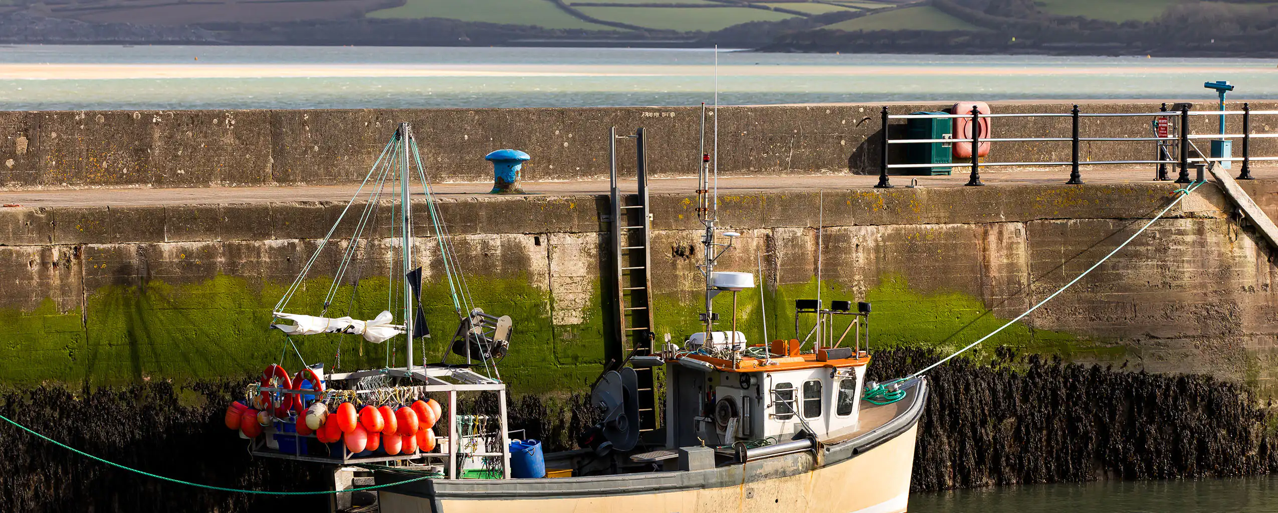 A fishing boat moored at Padstow Harbour, securely tied to the dock with calm waters surrounding it, Padstow was once know for it's fishing heritage.