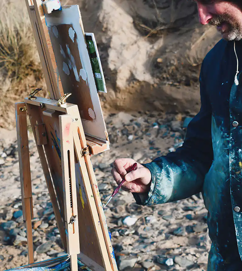 A man focused on painting a colourful scene on a canvas, Carbis Bay is know for its arts scene being so close to St Ives.