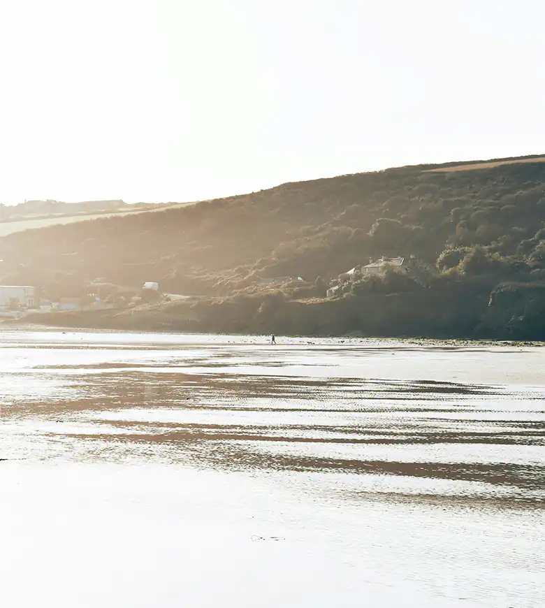 A beachgoer walks on Mawgan Porth Beach, as the surf and sand create a vibrant coastal scene.