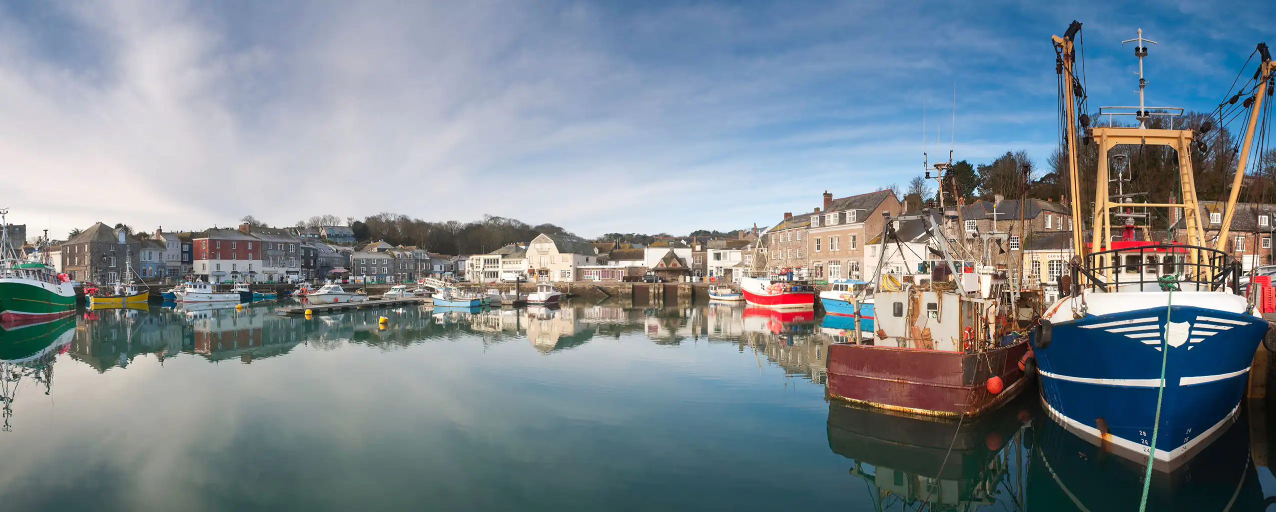 A panoramic view of Padstow Harbour, featuring several boats docked peacefully in the water, this area is know for some of the best food in Cornwall.