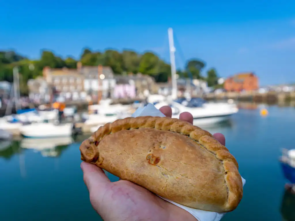 A person enjoys a pastry at Padstow Harbour, with boats and the marina visible in the background.