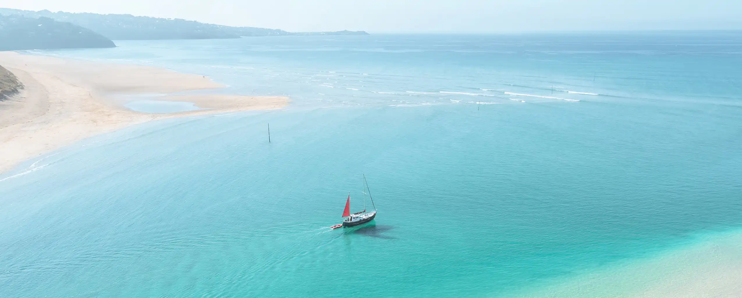 A boat gently floats on the calm waters of Hayle Estuary in Cornwall, surrounded by scenic natural beauty.