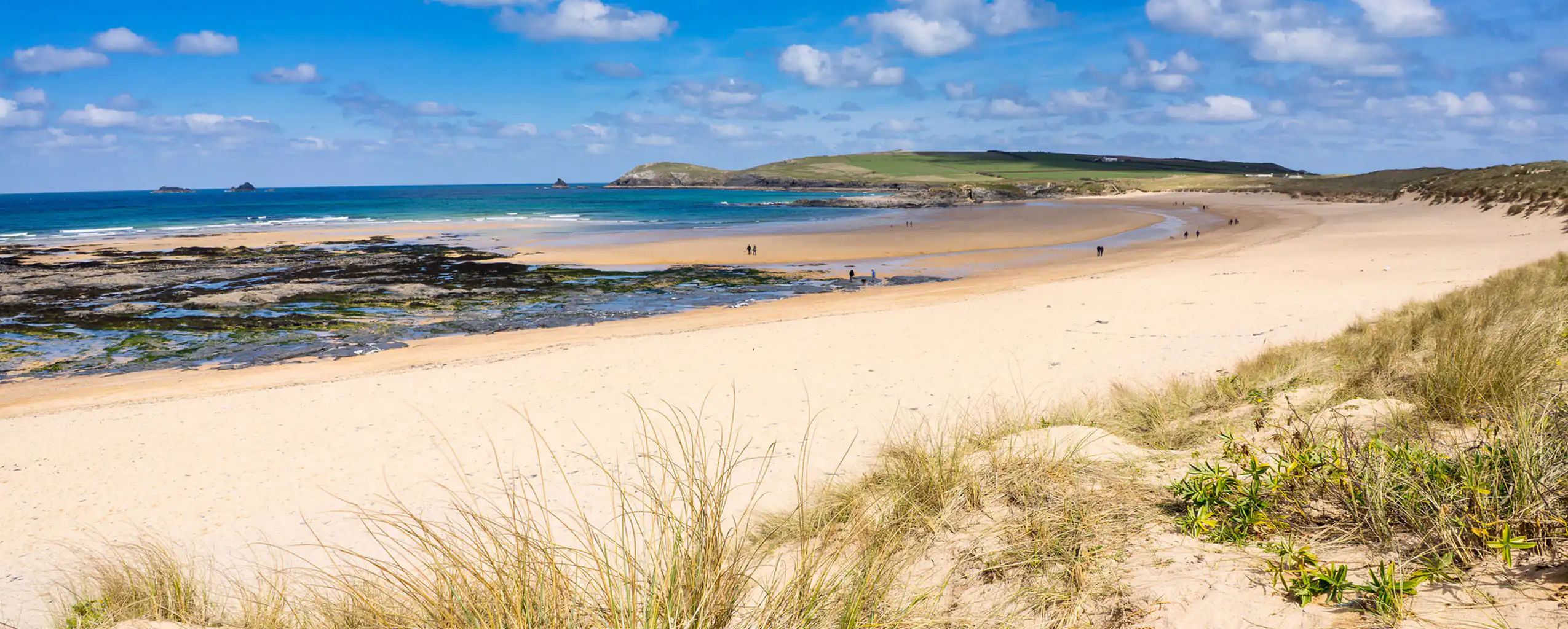 Sandy beach at Constantine Bay in Cornwall, with gentle waves lapping at the shore under a clear blue sky, a great to visit from a Cornwall cottage sleeping 4.