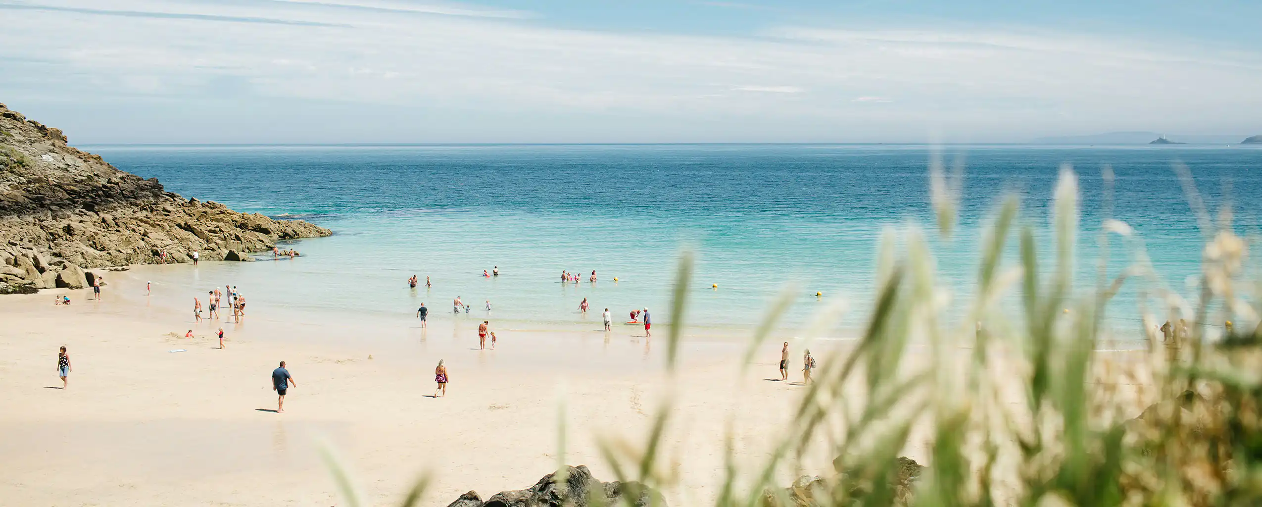 A lively group of people enjoying a sunny day at Porthgwidden Beach in St Ives, Cornish Escapes was founded in St Ives as well.