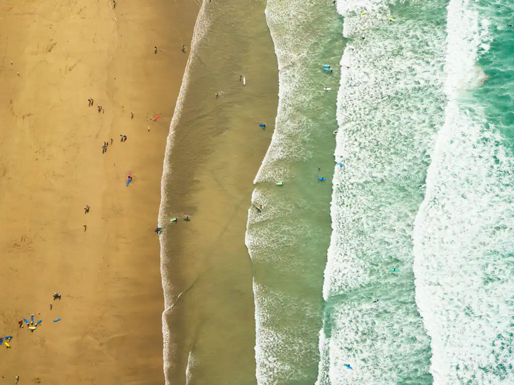 Aerial view of Fistral Beach in Newquay, showcasing people enjoying the surf and sun at a busy surf school, a great thing to see and do in Newquay.