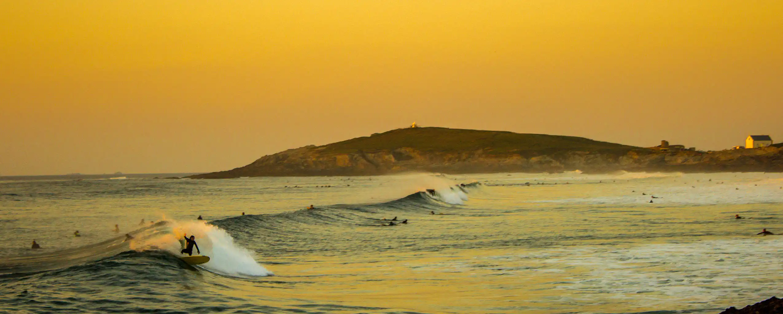 Fistral Beach glows yellow at sunset with waves lapping on the shore, a great view from our Newquay cottages with sea views.