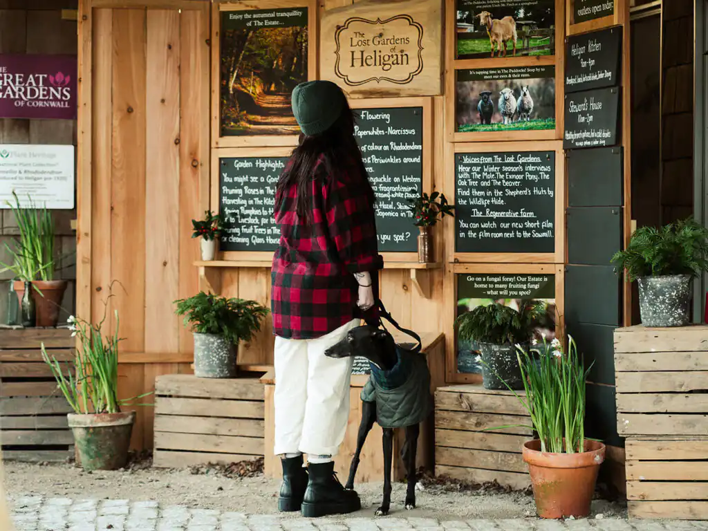 A woman and her dog are in front of a wooden sign, located at the Lost Gardens of Heligan, a great place to visit for a walking holiday in Cornwall.
