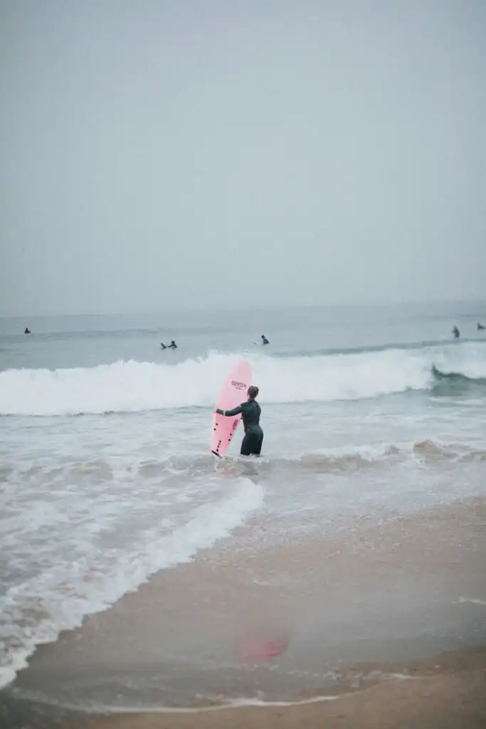 A person enters the ocean with a pink surfboard, embracing the rainy weather while surfing in St Ives.
