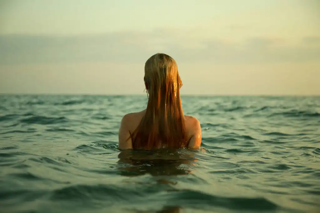 A woman with long hair splashes in the ocean, representing tranquillity and the joy of sea swimming in West Cornwall.