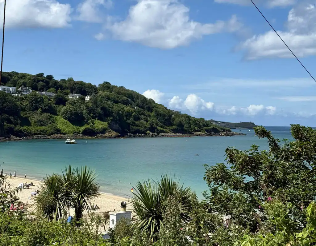 A sunny Carbis Bay Beach with a few people enjoying the sand and a green hill in the background, a great place to stay in Cornwall.