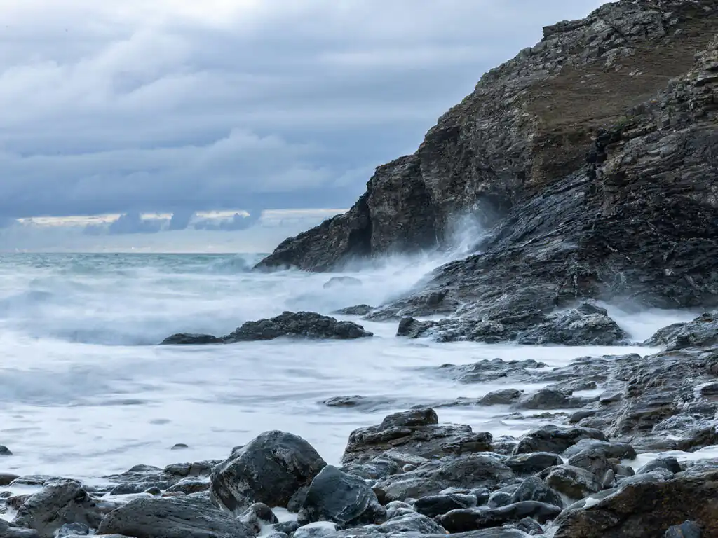 Rocky shoreline at Chapel Porth Beach in St Agnes, with waves crashing dramatically against the rugged rocks.