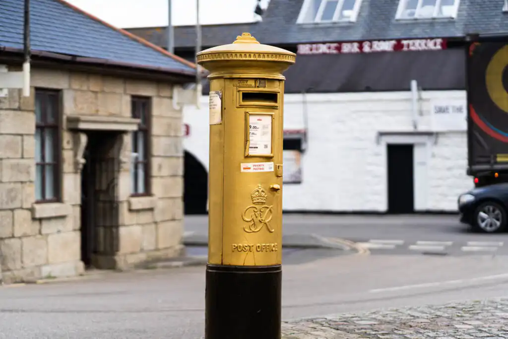 A golden post box at a street corner, honouring Helen Glover in Penzance, celebrating one of Cornwall's most famous women.