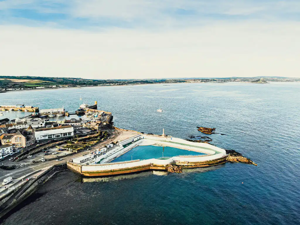 Aerial perspective of a quaint Penzance with the prominent Penzance Jubilee Pool, highlighting its recreational appeal, a great thing to do in Mounts Bay.