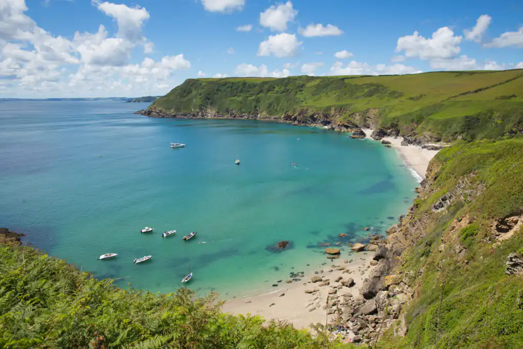 Lantic Bay Beach in Cornwall with turquoise waters, green cliffs, and small boats near the sandy shore, a great hidden beach in Cornwall.