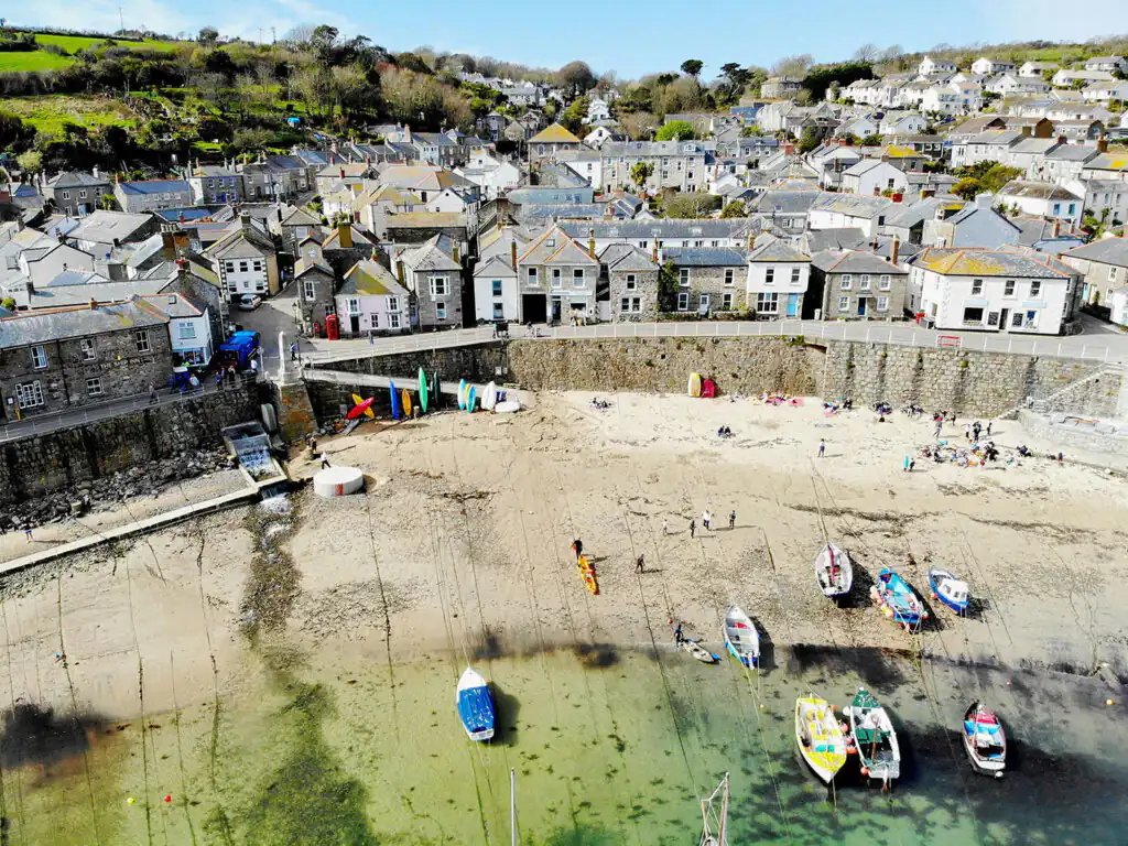 A scenic view of Mousehole Harbour, featuring a beach and boats in the picturesque area of Mounts Bay.