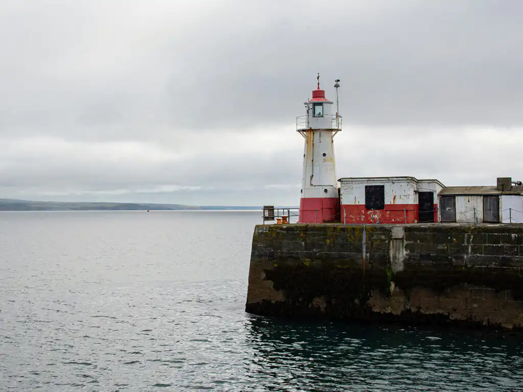 A striking lighthouse stands on a pier, overlooking the waters of Mounts Bay and Newlyn Harbour, a great thing to do in Mounts Bay.