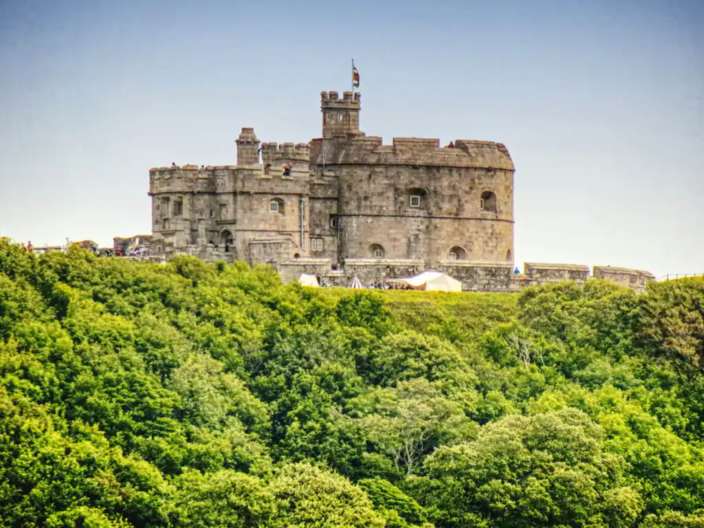 Pendennis Castle, in Falmouth, on a hillside with dense green foliage and a clear blue sky, a grand historic site in Cornwall.