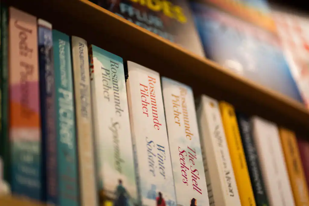 A bookshelf filled with various books, prominently featuring works by Rosamunde Pilcher, one of the most famous Cornish women.