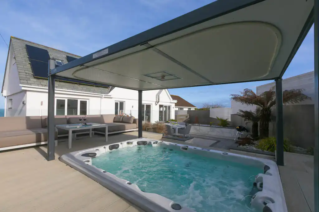 A cosy hot tub on a deck, sheltered by a roof at Solstice, perfect for family celebrations in Cornwall.