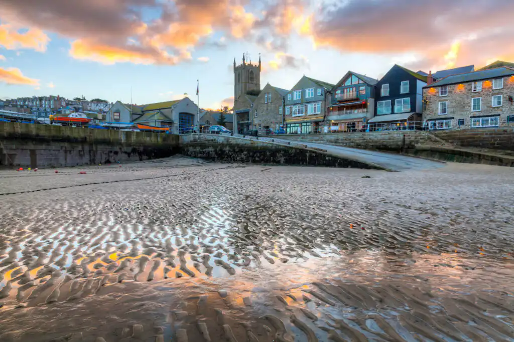 A sandy beach in St Ives with buildings nearby and a cloudy sky, perfect for walks ending with a roast.