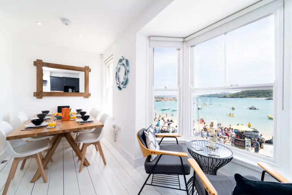 A cosy dining room with a large window showcasing a beautiful beach view at St Ives House, perfect for family celebrations in Cornwall.