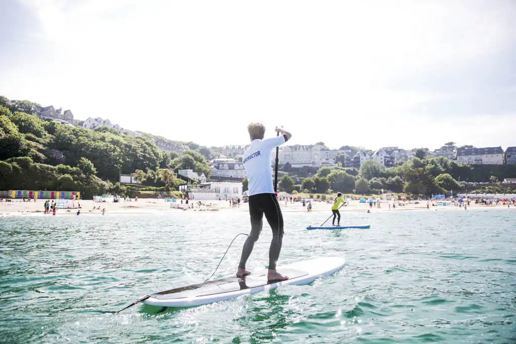 A surfer balances on a board amidst ocean waves, capturing the excitement of surfing lessons in St Ives, Cornwall, a great activity for holidays for large groups in Cornwall.