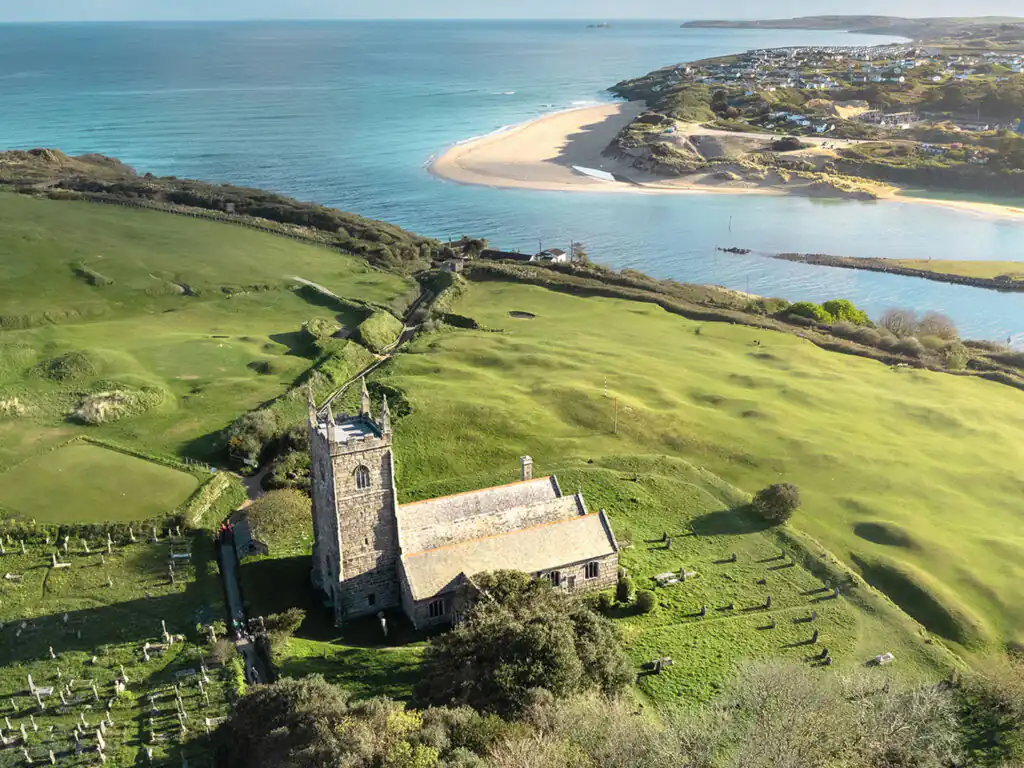 Aerial view of St. Uny Church in Lelant with surrounding graveyard and adjacent beach, just one of many locations that Cornish Escapes can help with holiday cottage ownership.
