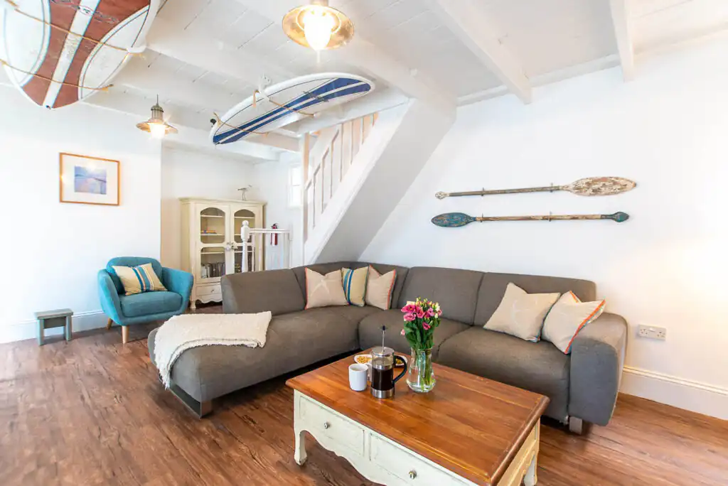 Stones Throw has cosy living room featuring a couch, coffee table, and a surfboard decoratively mounted on the wall. Perfect for dog-friendly breaks in St Ives.