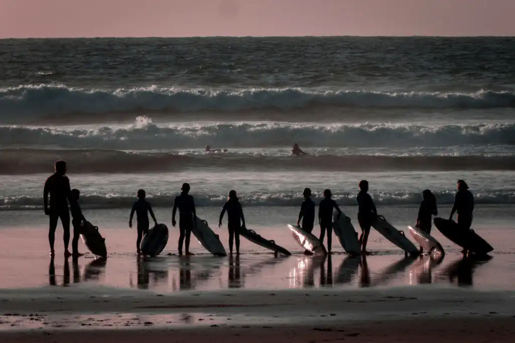 A group of people on the beach, smiling and holding surfboards, ready for a surfing lesson with a surf school in West Cornwall.