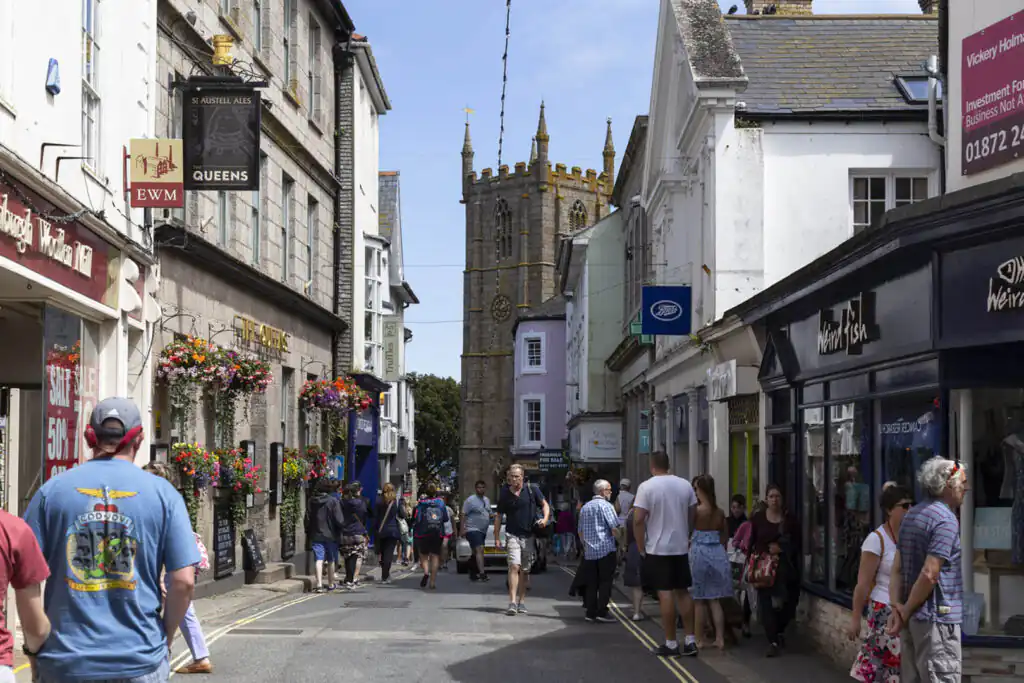 A group of people walks along a bustling street in St Ives, featuring The Queens, one of the best pubs and bars in St Ives.