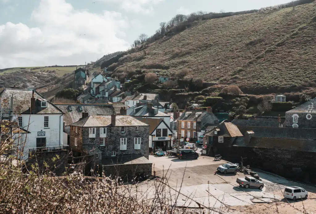 Coastal village view featuring Port Isaac Harbour, with a hill rising in the background and charming houses lining the shore. Port Isaac is a popular holiday cottage location.