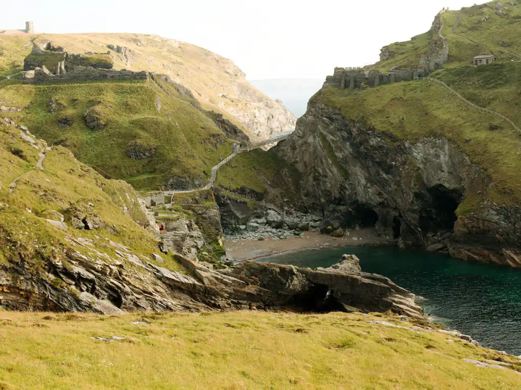 Grassy hillside overlooking Tintagel Castle ruins on cliffs, inviting exploration and scenic views when visiting from Mawgan Porth.