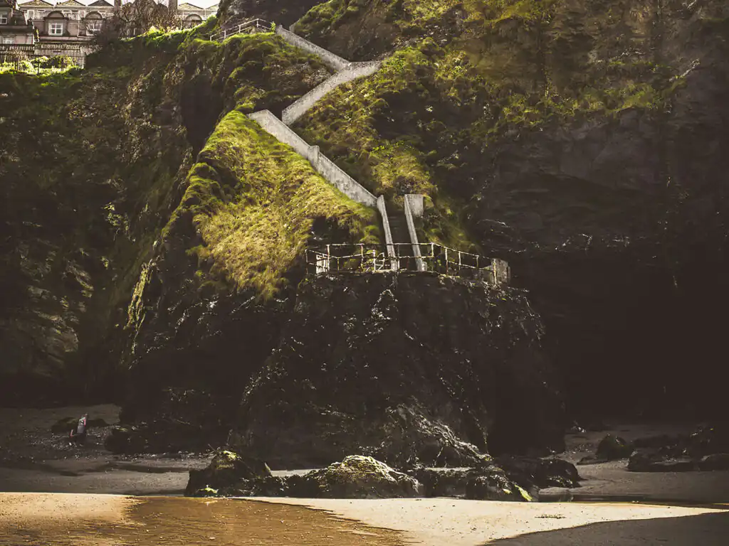 A scenic beach view featuring a staircase leading up to a cliff, showcasing Tolcarne Beach in Newquay, a great thing to do in Newquay off the beaten track.