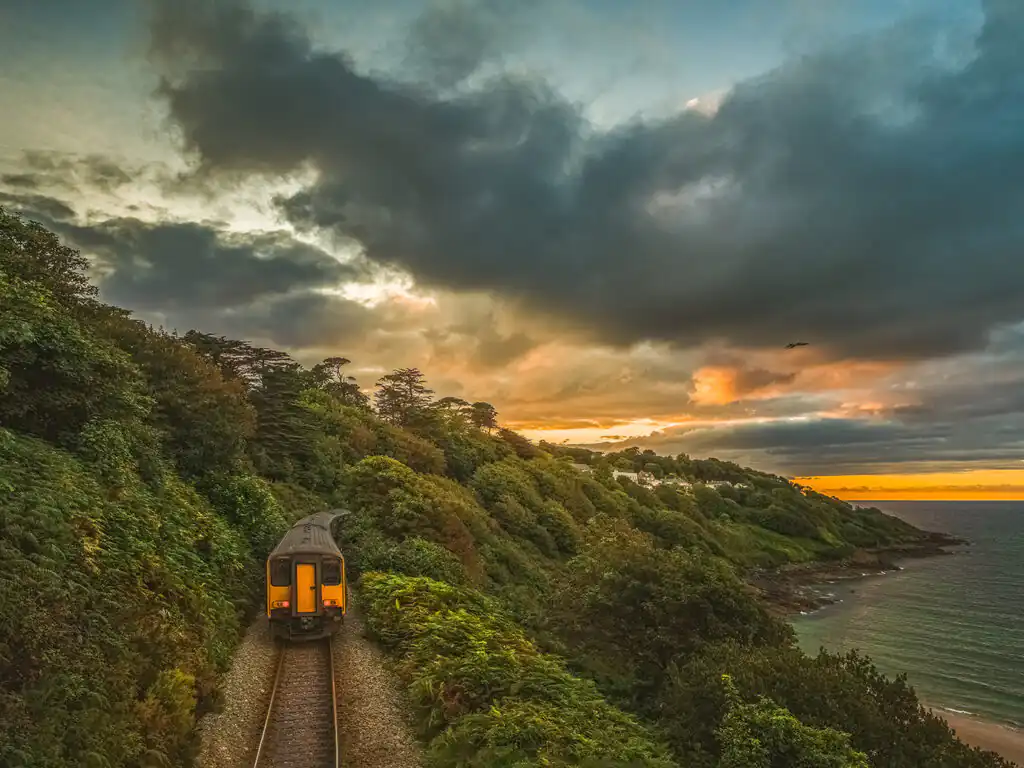 A train travels along the tracks beside the ocean in Carbis Bay, showcasing the scenic St Ives train line.