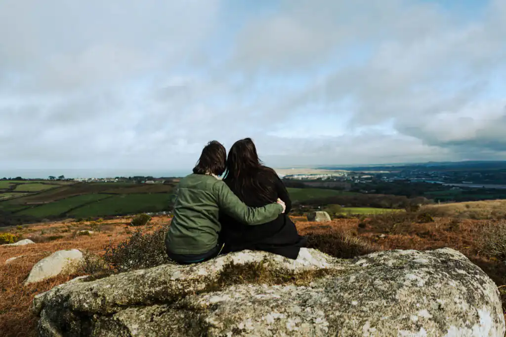 Two people sit on a rock, enjoying a scenic view of the valley on Valentine's Day at Trencrom Hill in Cornwall.