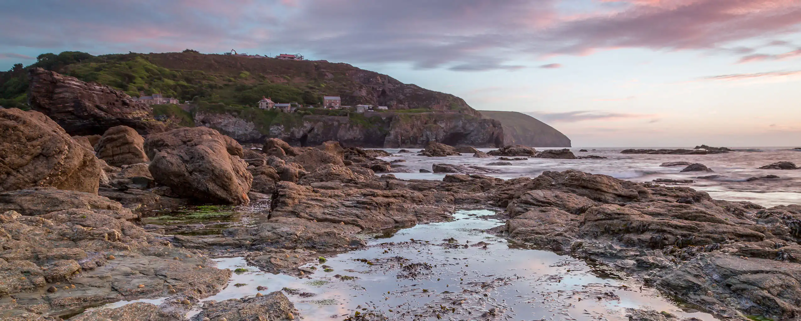 A rocky beach at Trevellas Porth near St Agnes, with water reflecting the vibrant colours of a sunset, a vibrant area for food and drink.