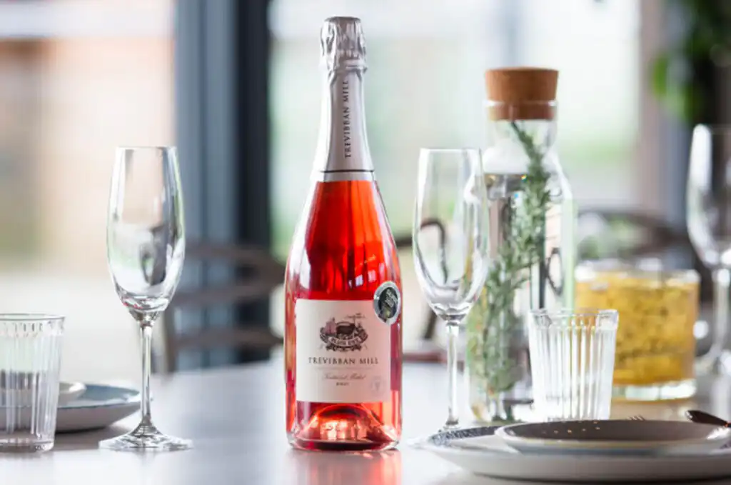 A bottle of pink wine on a table, accompanied by glasses and plates, showcasing Cornish Trevibben Mill Winery's offerings, one of the best Cornish Wineries and Vineyards to visit.