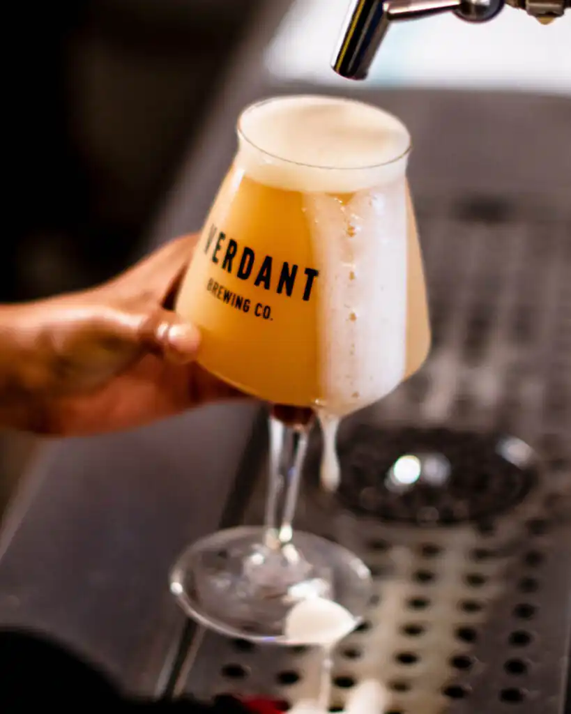 A person fills a glass with a refreshing beer, featuring a pint from Verdant Brewing Co, one of the best breweries in Cornwall.