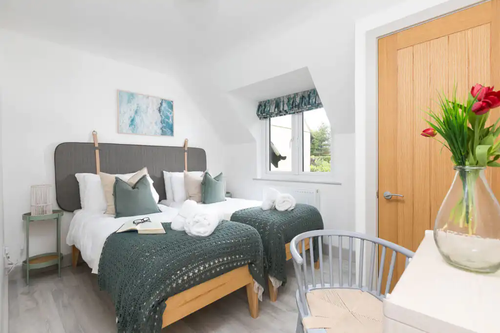 Two cosy beds in a charming bedroom with a wooden door, showcasing the inviting second bedroom at Westholme, St Ives.