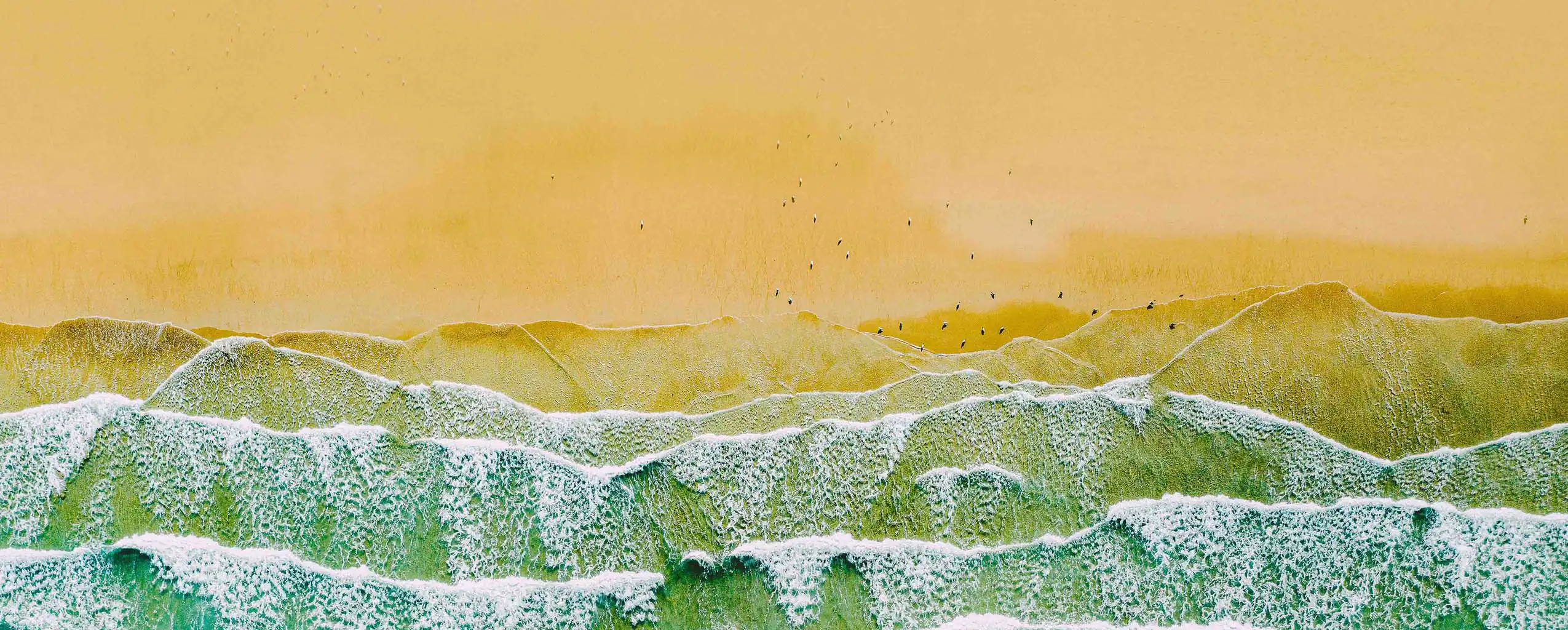 Colourful waves crash against a bright yellow backdrop, at Carbis Bay beach, capturing the essence of Carbis Bay's coastal beauty.