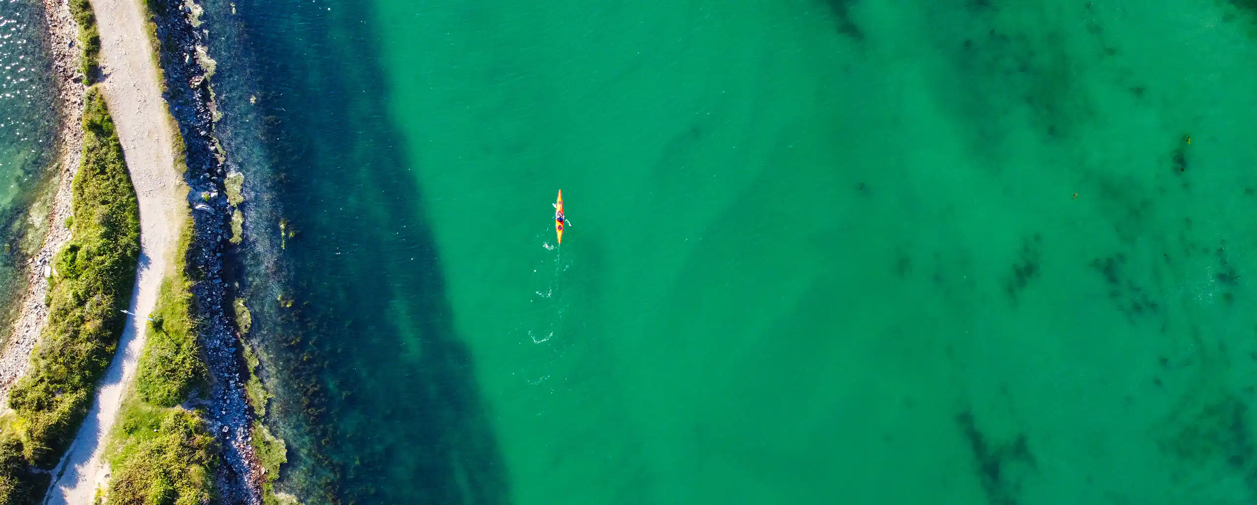 Aerial view of a kayak gliding through the tranquil waters of Hayle Estuary, surrounded by lush greenery, a part of Hayle's rich heritage.