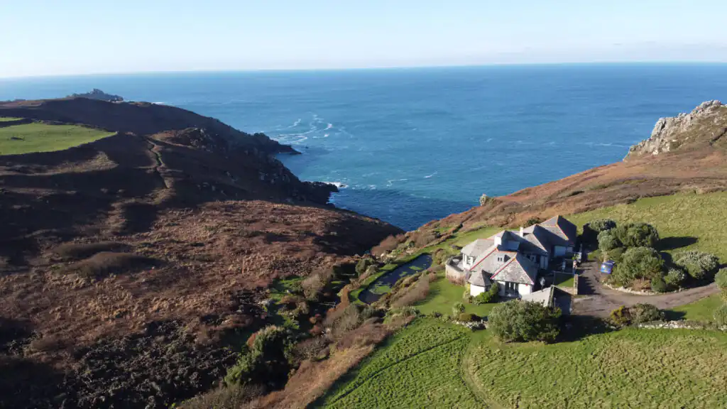 Aerial view of a house on a hill, overlooking the ocean near Zennor, showcasing the beauty of St Ives, a great place to visit during a day in St Ives.