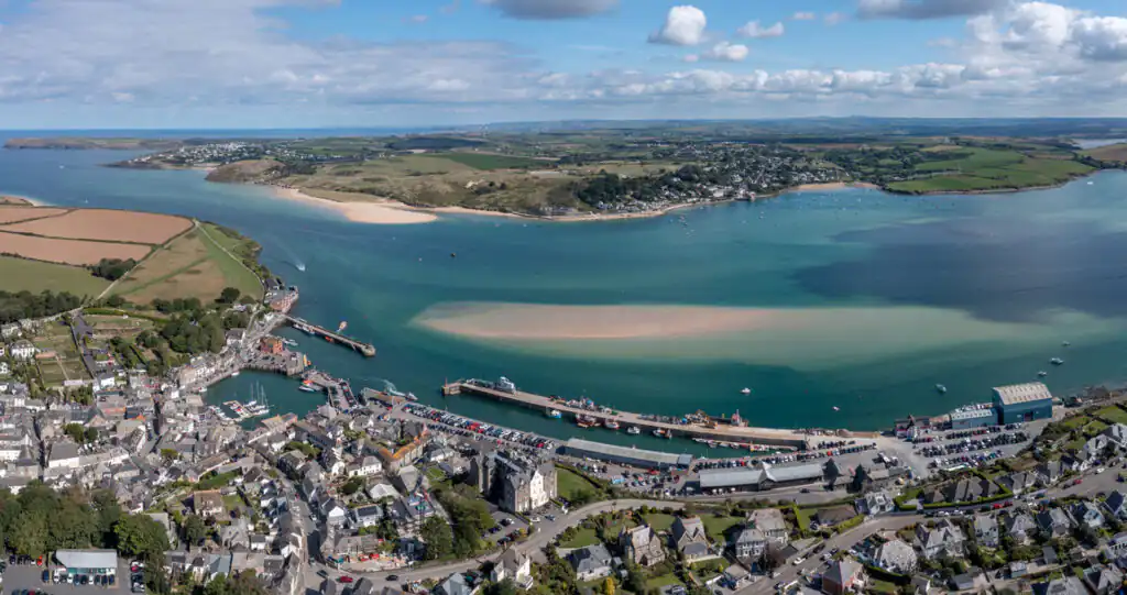 Aerial view of Padstow, Cornwall, showing buildings, a harbour, and the wide expanse of the Camel Estuary with a sandbar, a great place for a boat trip in Cornwall.
